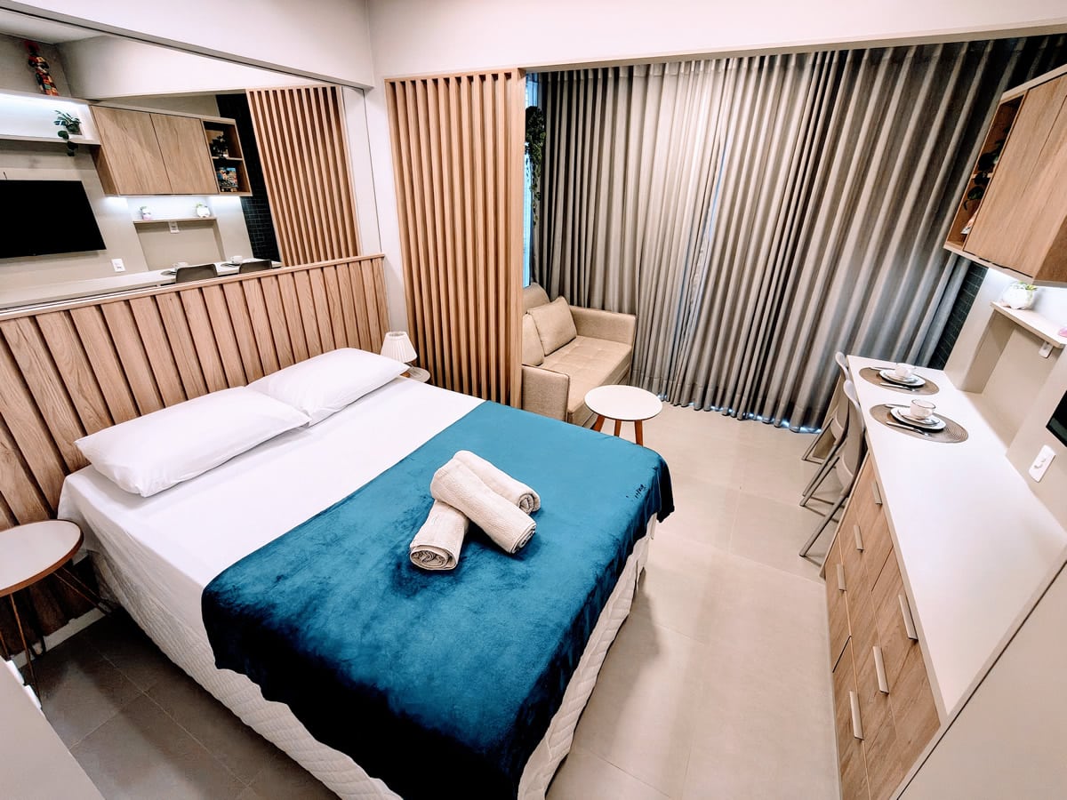 Interior do Studio 305 no Barra Conceito com cama de casal, sofá, bancada e decoração moderna