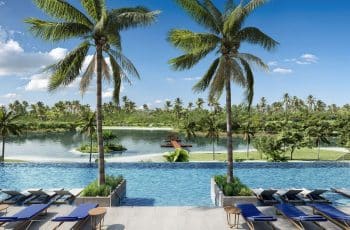 Vista panorâmica do acesso à piscina do Sauípe Lagoa Residence, ladeado por dois coqueiros majestosos.