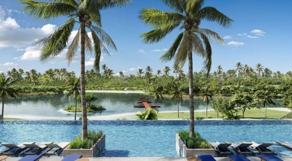 Vista panorâmica do acesso à piscina do Sauípe Lagoa Residence, ladeado por dois coqueiros majestosos.