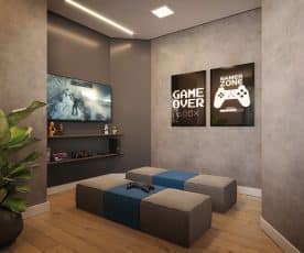 Uma sala de jogos moderna com paredes cinzentas, uma grande TV exibindo um jogo de vídeo, pufes confortáveis no chão e quadros temáticos de jogos na parede.
