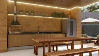 Área de churrasqueira com acabamento em madeira clara, bancadas em mármore preto, eletrodomésticos modernos, e iluminação de LED, criando um ambiente acolhedor e perfeito para encontros sociais.