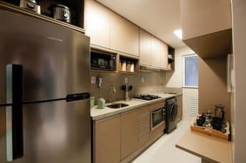 Cozinha compacta e funcional com eletrodomésticos modernos, armários em tons neutros e bancada de granito.