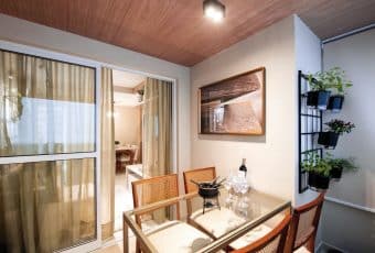 Varanda aconchegante do apartamento com mesa de jantar, cadeiras elegantes, decoração com plantas e uma bela vista para a sala de estar.