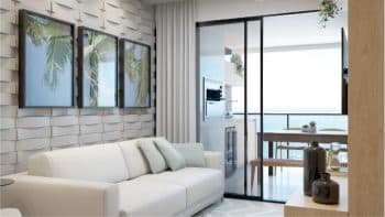 Sala de estar do Jaguaribe OCEAN SIDE com sofá branco, parede com textura geométrica e ampla porta de vidro que se abre para uma varanda com vista para o oceano.