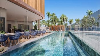 Área de piscina do BOSSA Farol de Itapoan com borda infinita, vista para palmeiras tropicais, mobiliário em azul e área de descanso coberta.