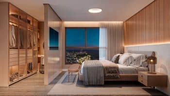 Suíte master elegante com cama de casal, closet integrado e uma grande janela com vista panorâmica noturna da costa urbana.