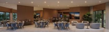 Interior do espaço gourmet no BOSSA Farol de Itapoan com mobiliário moderno em tons de azul e cinza, grandes mesas para refeições, decoração com plantas e vista para jardins externos.