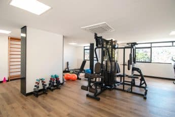 Academia moderna com equipamentos de musculação, pesos livres, bolas de exercício e piso de madeira.