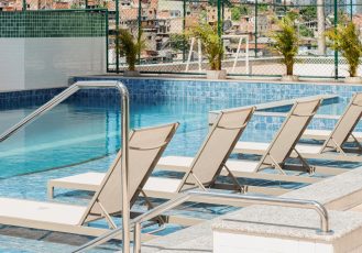 Espreguiçadeiras submersas em uma piscina, com degrau de acesso em primeiro plano e plantas decorativas ao fundo.