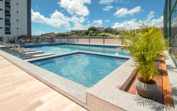 Piscina infantil e adulto em área externa, com espreguiçadeiras submersas, deck de madeira e plantas decorativas ao redor.