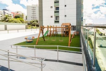 Parque infantil com balanços, escorregador, casinha de madeira, gira-gira e piso de grama sintética.