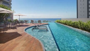 Piscina com raia infinita no MOOD Costa Azul, rodeada por espreguiçadeiras e mesas com guarda-sóis, com vista panorâmica para o mar.