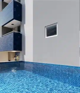 Imagem da piscina do Jardim das Tulipas, destacando um espaço de lazer elegante com água cristalina, borda em azulejo azul e área de convivência ao fundo.