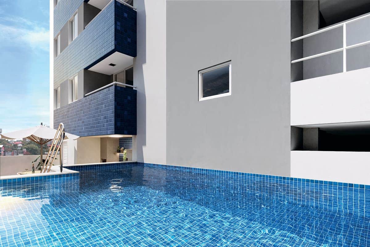 Imagem da piscina do Jardim das Tulipas, destacando um espaço de lazer elegante com água cristalina, borda em azulejo azul e área de convivência ao fundo.