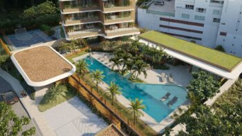 Vista aérea da piscina com solário, espreguiçadeiras, vegetação tropical, quadra esportiva e fachada do Elleve Horto ao fundo