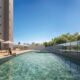 Piscina adulto com deck e espreguiçadeiras no Sevilha Residencial, cercada por vegetação e vista urbana