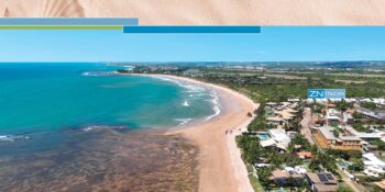 Imagem aérea panorâmica de Itacimirim destacando a localização do ZN Itacim, com mar azul, recifes, faixa de areia e vegetação nativa ao fundo.