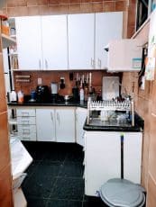 Cozinha do apartamento usado 3 quartos no Garcia, Salvador, com armários brancos planejados, bancada em granito preto e piso em mármore escuro.
