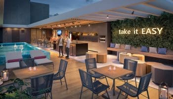Área de lazer do Easy São Lázaro em Salvador, com piscina iluminada, lounge gourmet moderno, mesas externas e parede verde com letreiro "take it EASY".