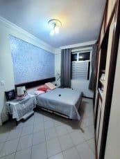 Suíte do apartamento usado 3 quartos no Garcia, em Salvador, com cama de casal, mesa lateral decorada, cortinas e parede com detalhe em textura.