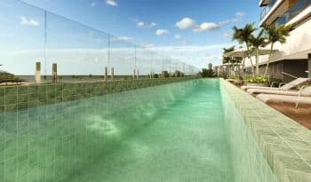 Piscina com deck e raia de 20 metros do Laut Jaguaribe, cercada por guarda-corpo de vidro e com vista panorâmica para o mar de Salvador.