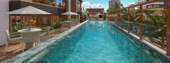 Piscina do Vivid Pituba com deck molhado, guarda-corpo em vidro e mesas com ombrelones