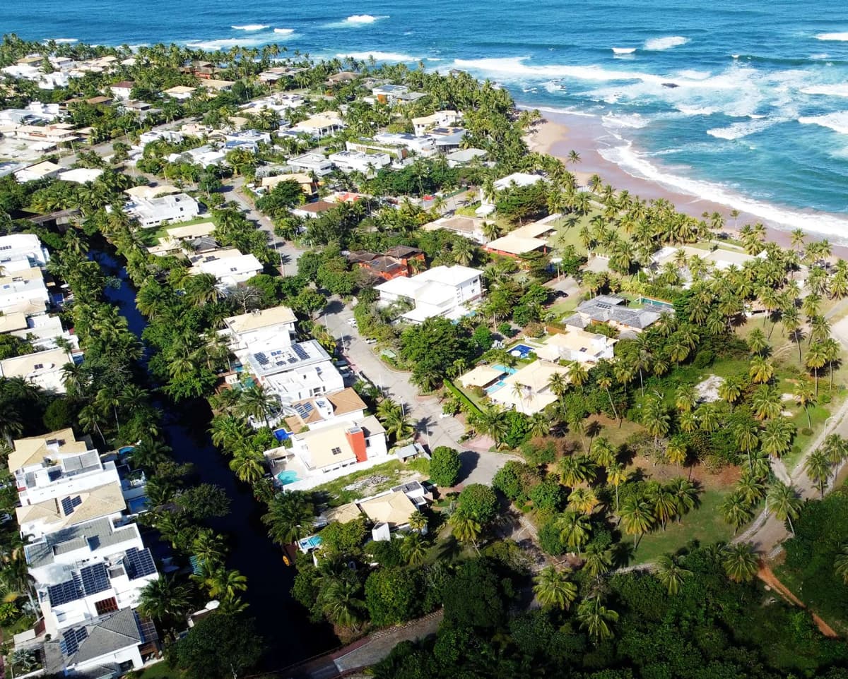 Vista aérea do condomínio Busca Vida mostrando casas de alto padrão, área verde preservada e a praia logo à frente.