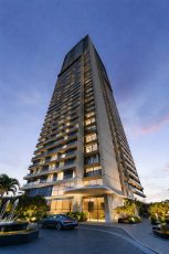 Fachada do edifício Beach Class Bahia, torre residencial moderna com varandas, iluminação cênica, paisagismo e acesso porte-cochère na entrada principal